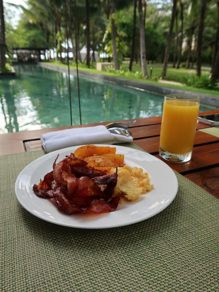 Breakfast plate with bacon, eggs, orange juice by the pools at The Kempinski Bali